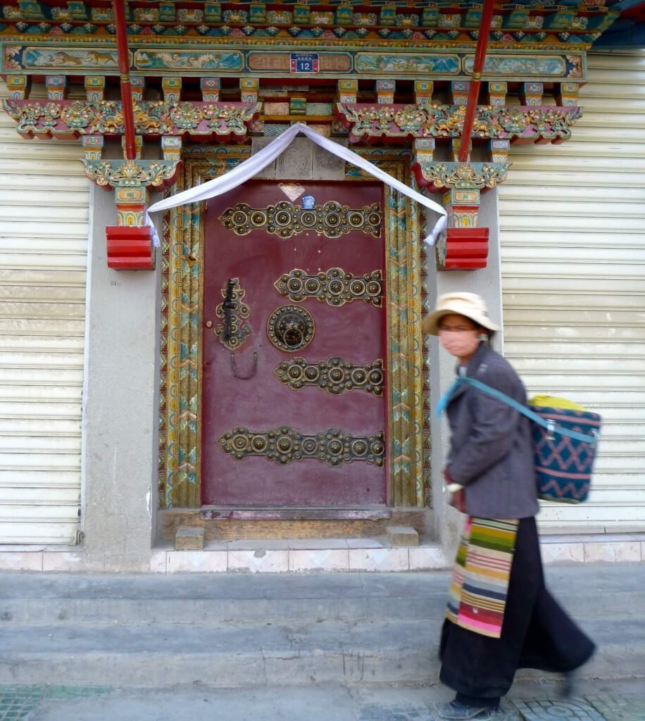 Vibrant Tibetan monastery door with detailed woodwork, ornate decorations, traditional patterns, and a woman in local dress walking past, capturing cultural heritage and immersive travel.