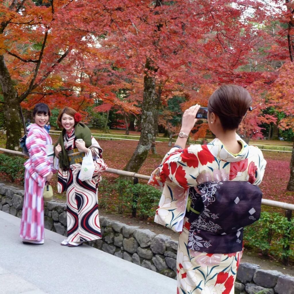 Beautiful women in traditional kimonos taking pictures during fall foliage season.