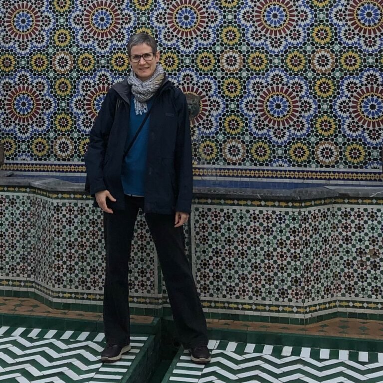 Experienced traveler enjoying Moroccan tile art, wearing practical outdoor gear against a stunning backdrop of traditional mosaic wall. Ideal for travel inspiration and cultural photography.