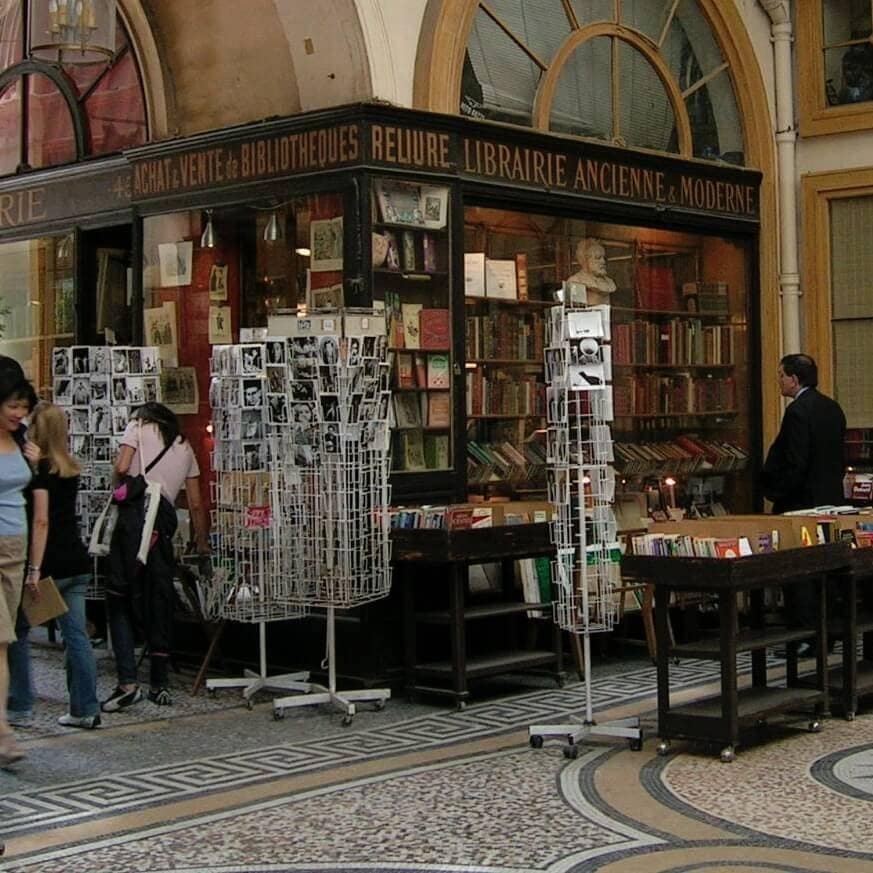 A charming bookstore in Paris showcasing vintage and modern books, with outdoor displays of postcards and a cozy, inviting atmosphere for book lovers and travelers.