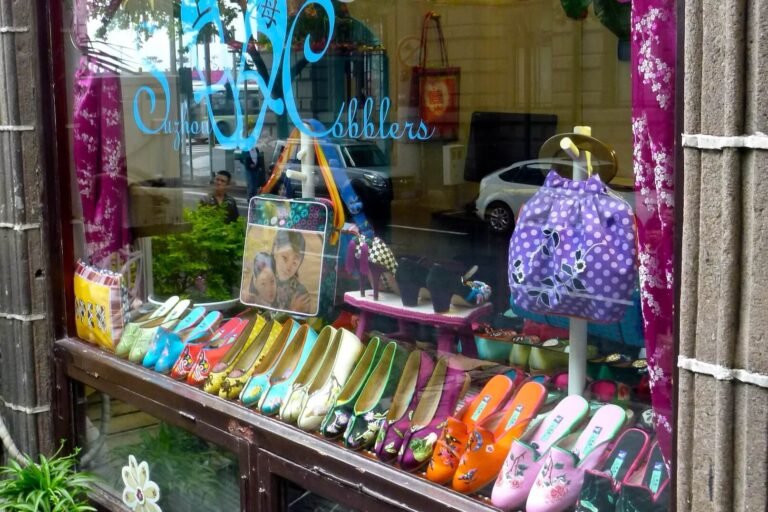 Embrace your creative mindset while enjoying brightly colored women's shoes, handbags, and accessories displayed in a quaint Shanghai shop window with a reflection of street and pedestrians outside.